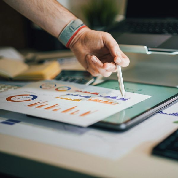 A hand holding a stylus pointing at colorful charts on a tablet.