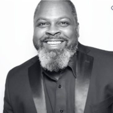 Smiling man in a tuxedo with a gray beard.
