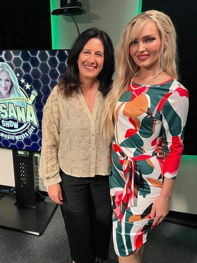 Two women posing happily in a studio with a colorful dress and a show display in the background.