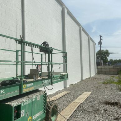 Construction lift near a freshly painted white wall on a gravel surface.