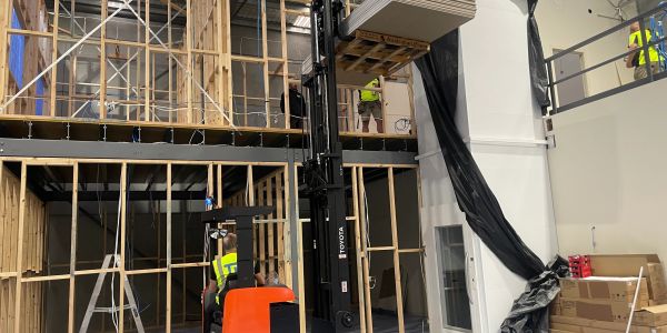 Workers using a forklift to install equipment in a construction site.