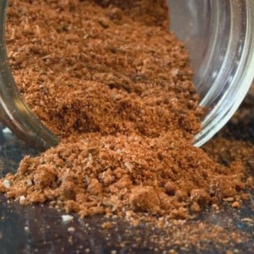 Close-up of brown spice powder spilled from glass jar.