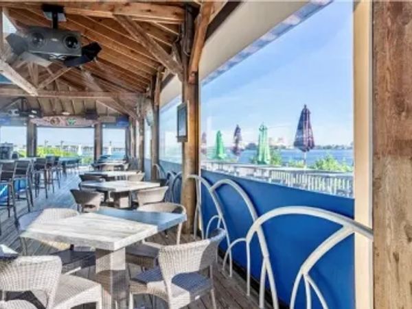 Outdoor wooden deck restaurant with waterfront views and wicker chairs.