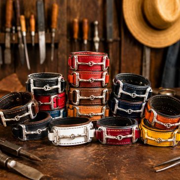 Stack of colorful leather horse bit bracelets with metal buckles on a wooden table.