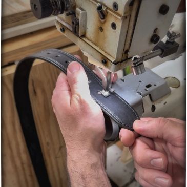 An Amish craftsman sewing a black leather belt.