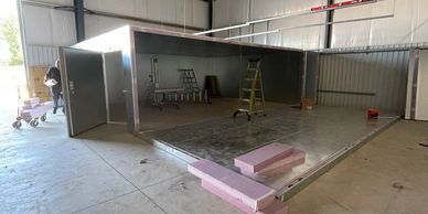 Partially constructed metal structure inside a workshop with tools and insulation foam.