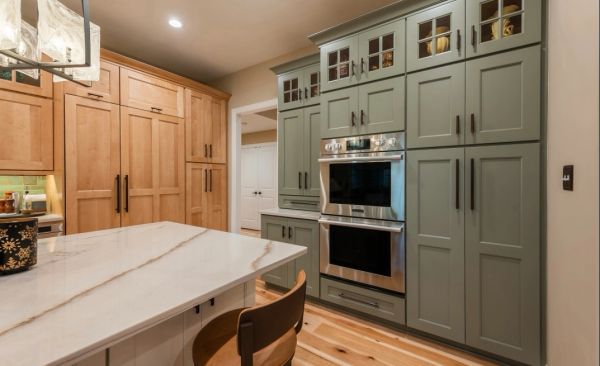 Modern kitchen with green and wood cabinetry and marble countertop.