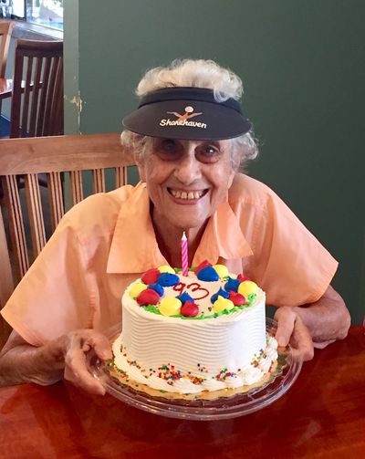 Elderly woman smiling with a birthday cake and single candle.