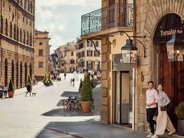 Couple walking out of a historic building on a sunny street in a European city.