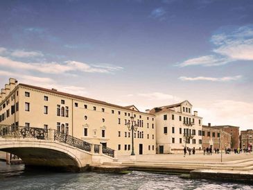 Historic building by a canal with a stone bridge under a cloudy sky.