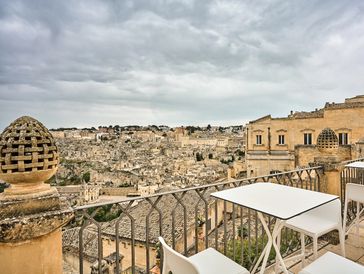 View of an ancient city from a balcony with white tables and chairs.