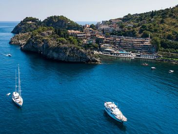 Yachts sailing near a coastal town with rocky cliffs and greenery.
