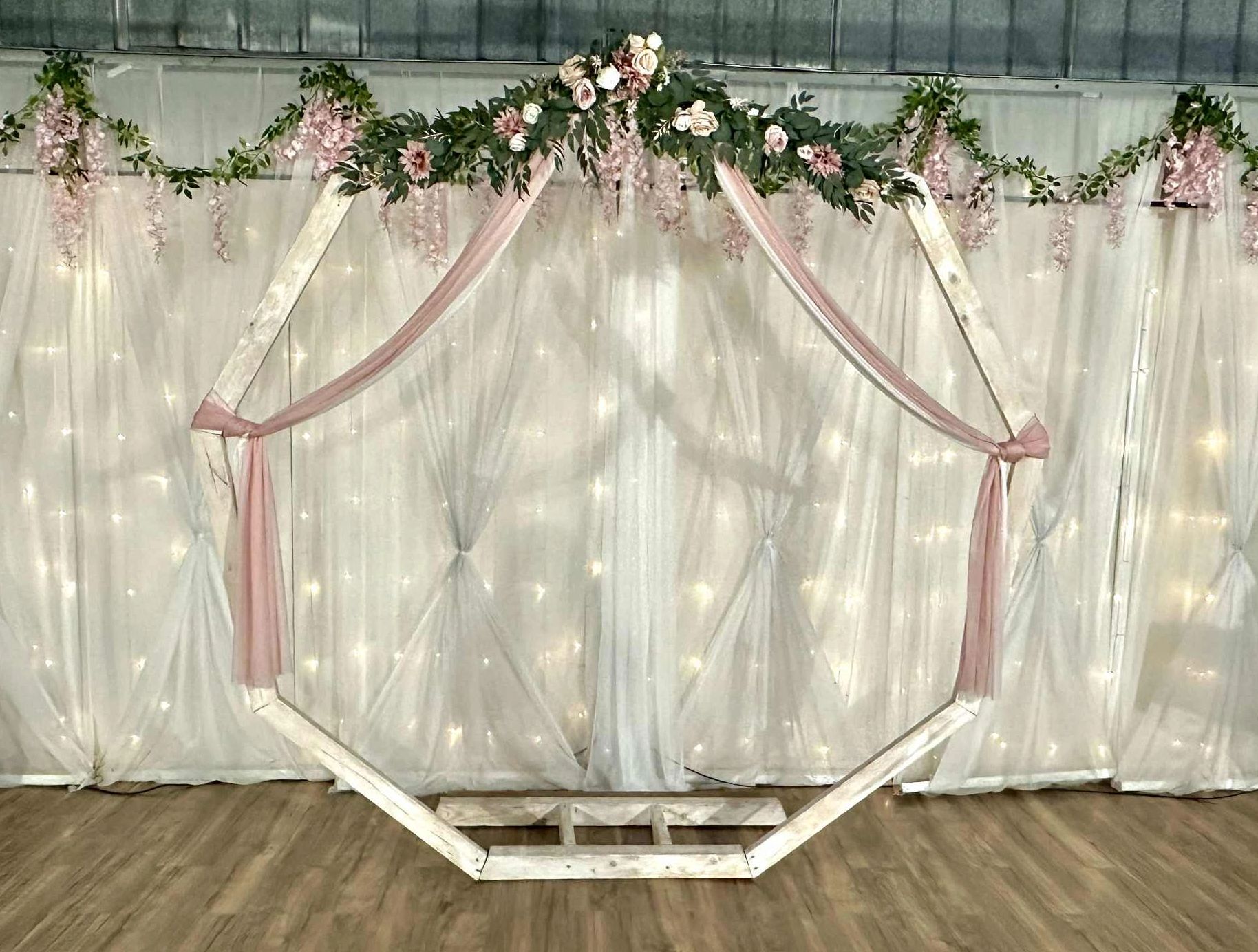 Wedding ceremony backdrop with arch, draping, florals and twinkle lights