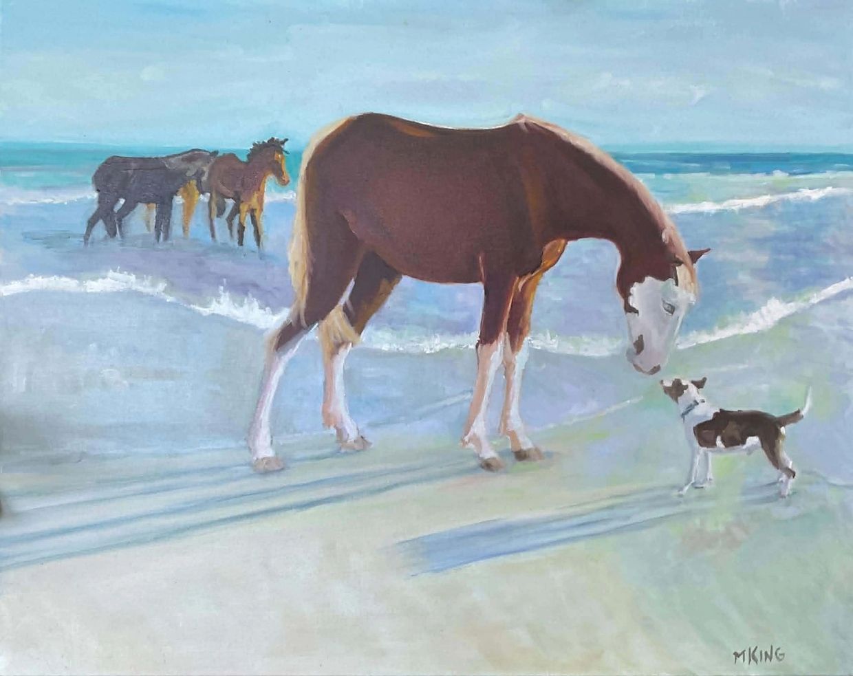 A horse and dog meet on a beach with three horses in the background.