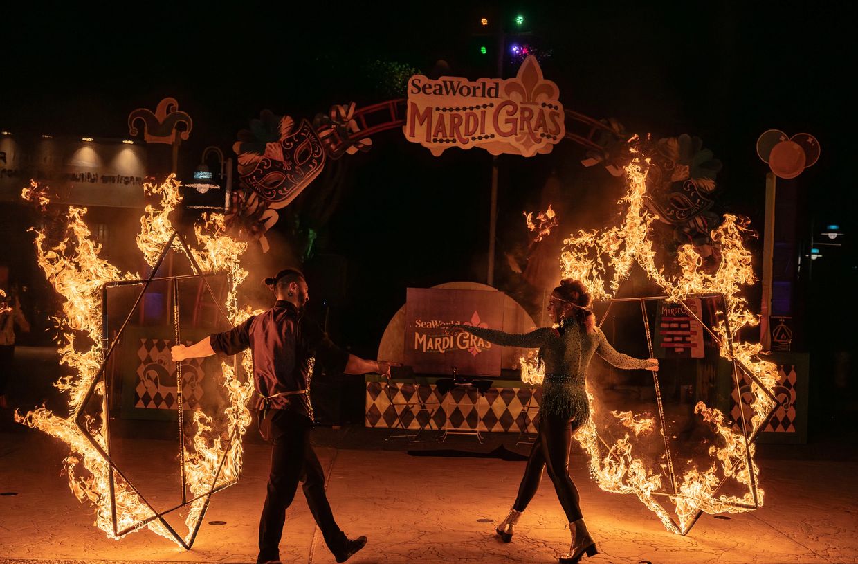 Two performers with flaming props at SeaWorld Mardi Gras event at night.
