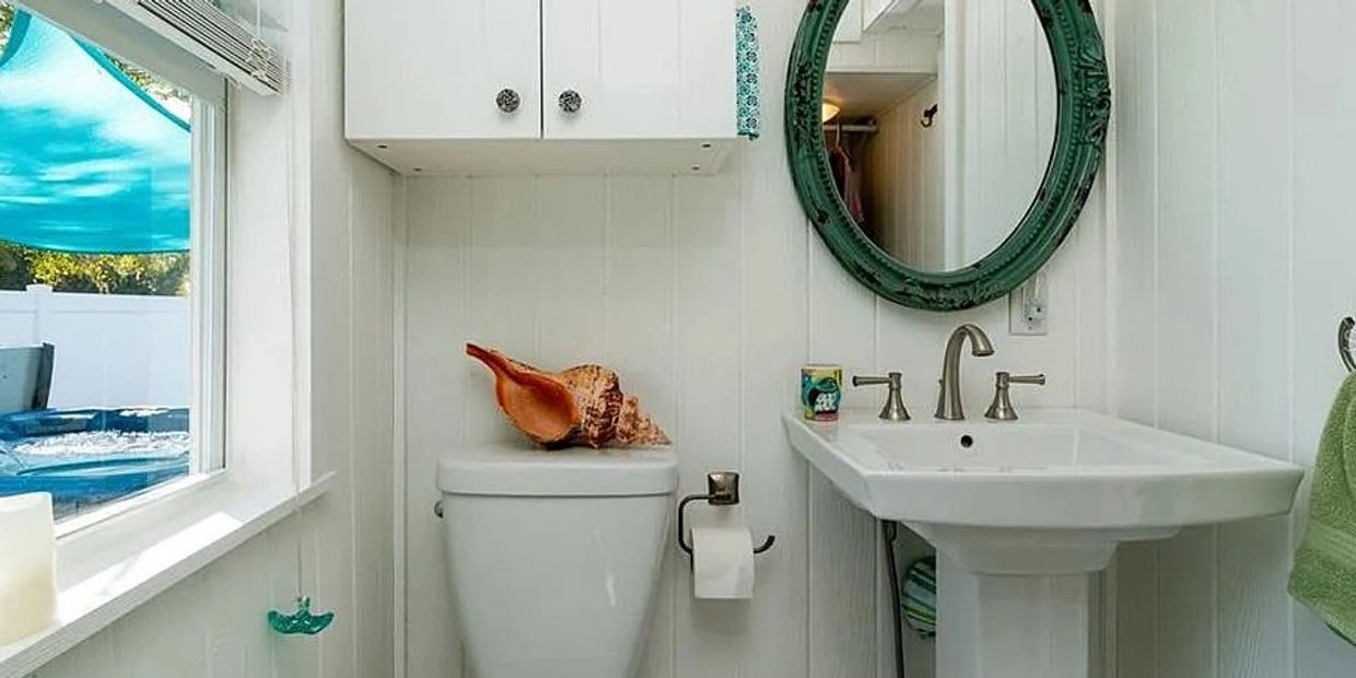 My tiny bathroom shows a sink a movable mirror, and a toilet, with beach accessories.