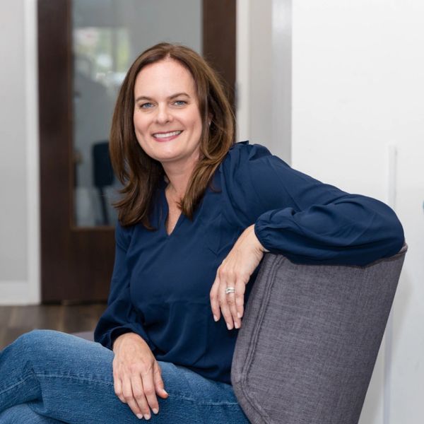Smiling woman in a blue blouse sitting on a chair indoors.