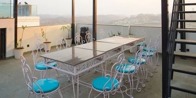 Outdoor dining area with white wrought iron chairs and blue cushions on a rooftop.