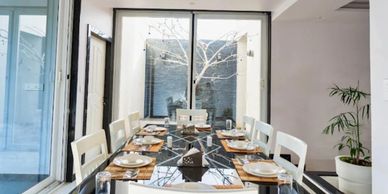 Modern dining room with a glass table and white chairs overlooking a small courtyard.