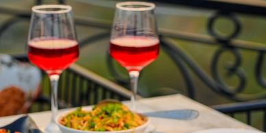 Two glasses of red wine with a bowl of pasta on a table.