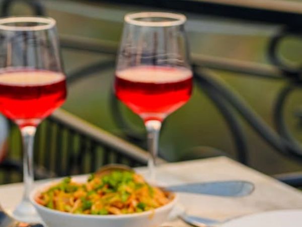 Two glasses of red drink with a bowl of food on a table.