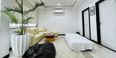 Minimalist living room with white walls, beige sofa, black beanbag, and indoor plant.