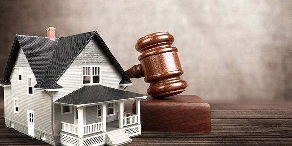 A house model next to a wooden judge's gavel on a table.
