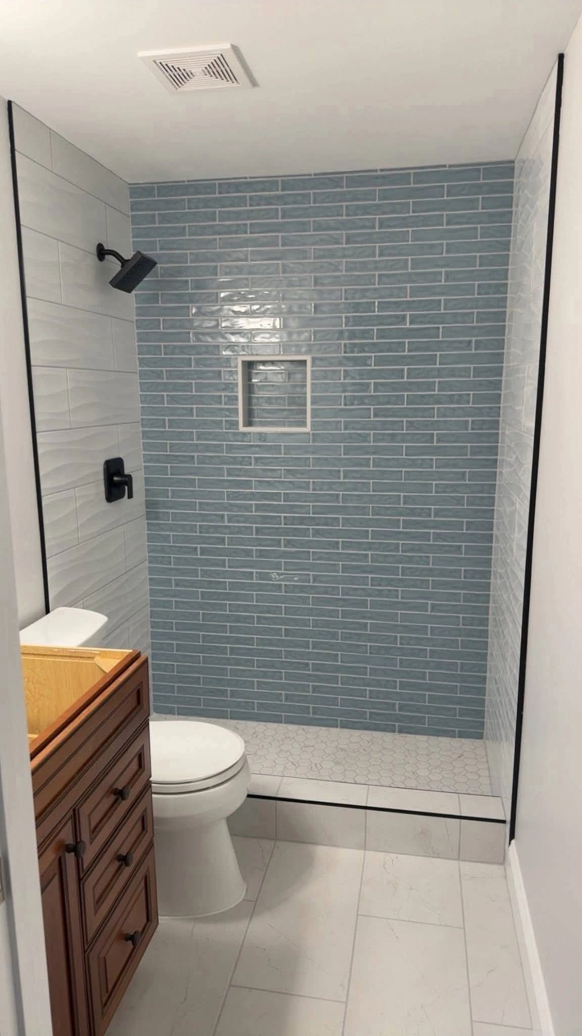 Modern bathroom with blue tiled shower and wooden vanity.