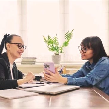 Two women sharing a moment while looking at a phone in an office.
