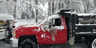 Red truck covered in snow during snowfall.