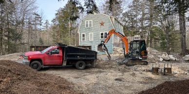 Excavator unloading earth into a dump truck on a forested construction site.