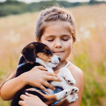 A young girl lovingly hugs a small puppy outdoors in a field.