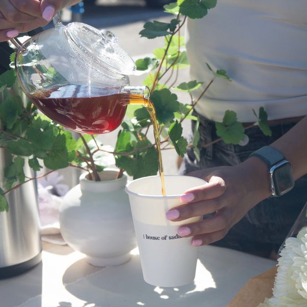 Pouring tea from a glass teapot into a white cup outdoors.