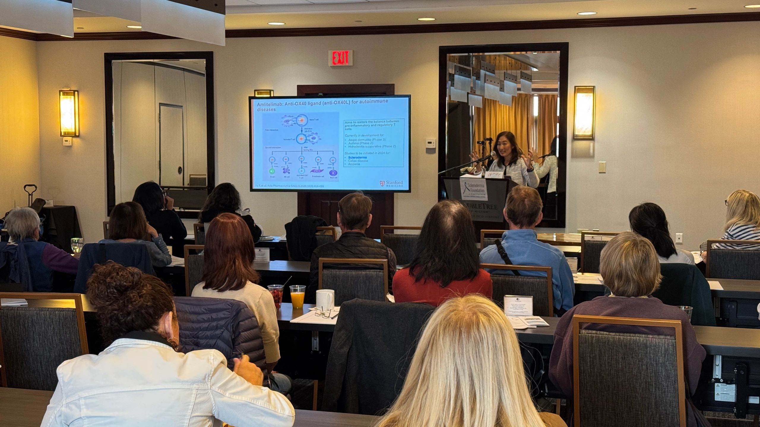 Audience attending a medical lecture on autoimmune diseases by a speaker at a podium.