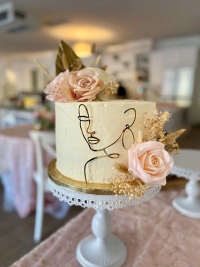 Elegant cake with minimalist face outline and floral decorations on a white stand.