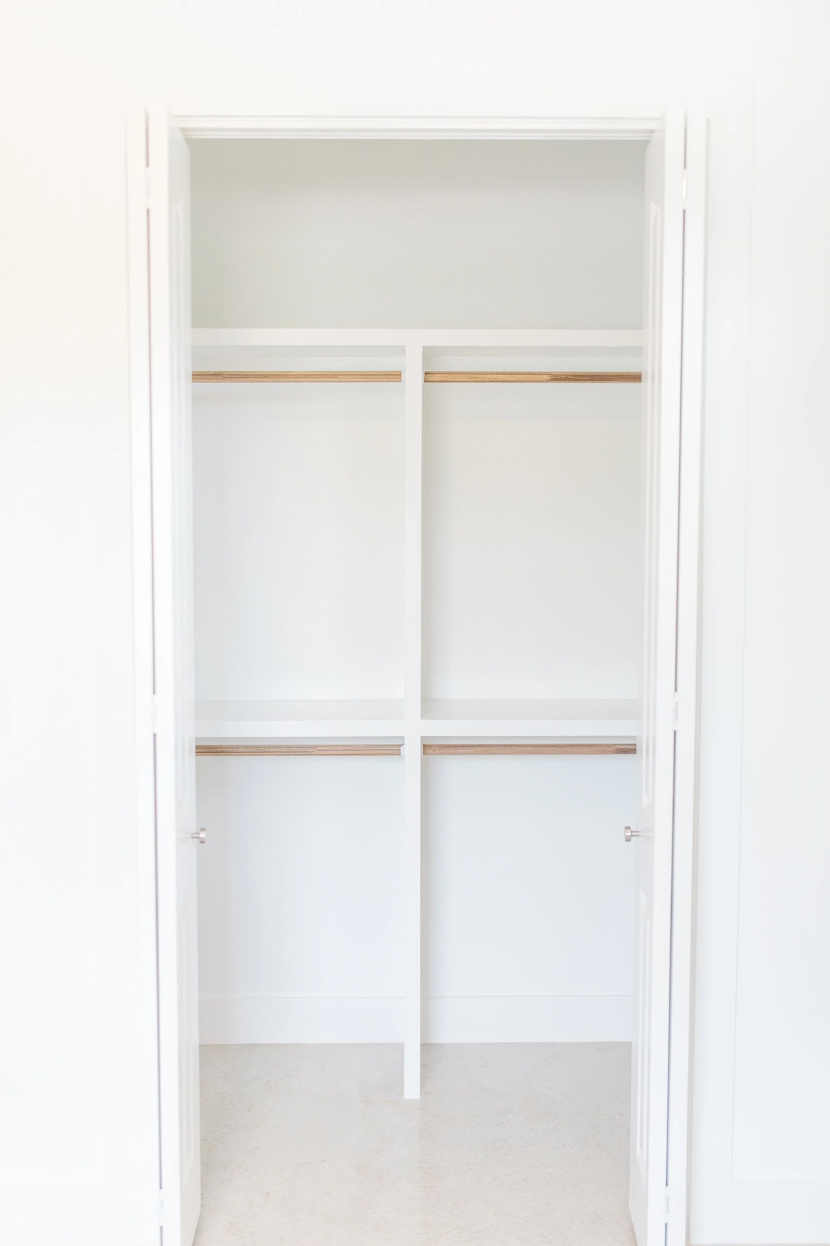 Empty white closet with wooden rods and shelves.