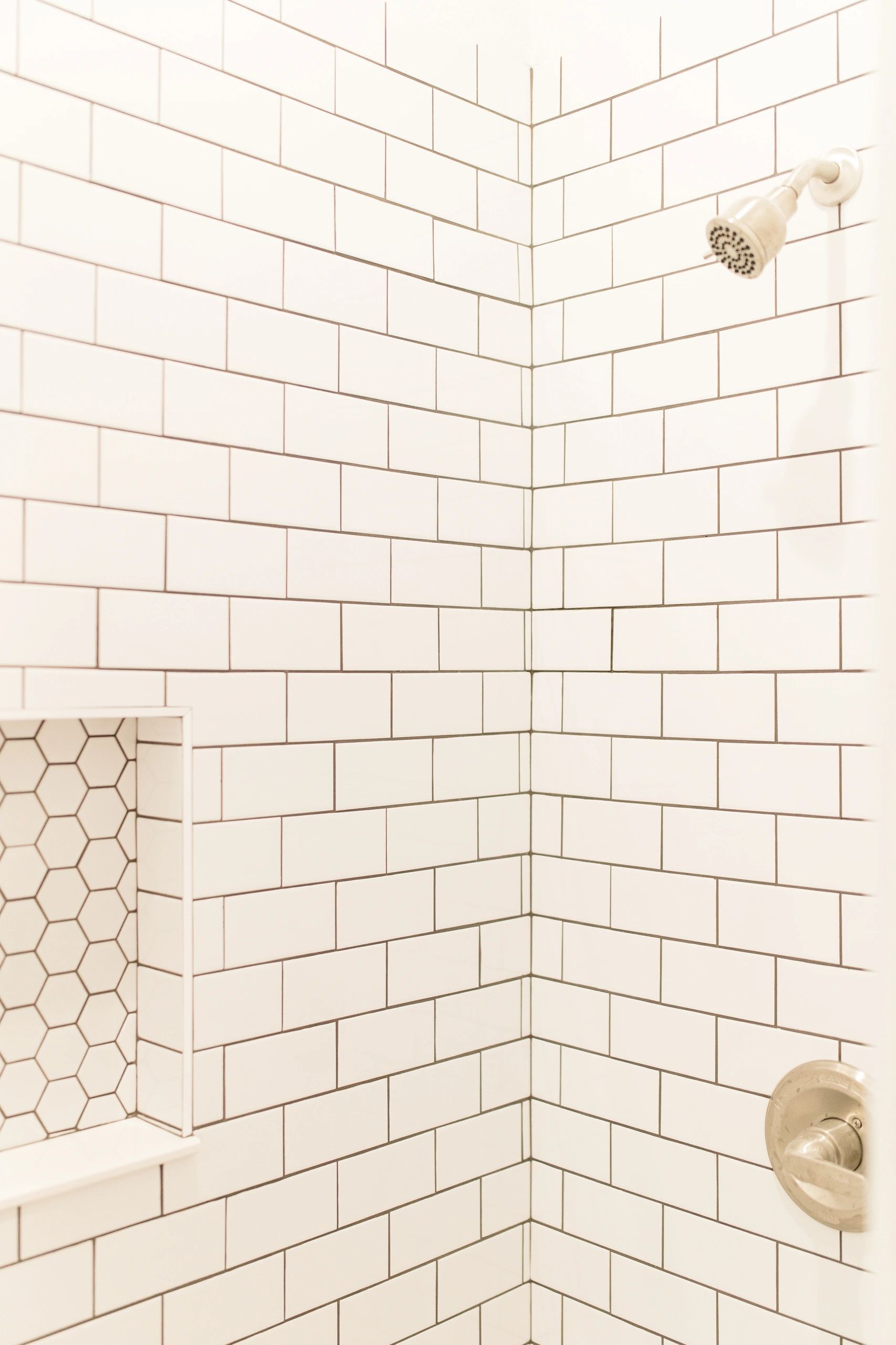 White tiled shower corner with hexagonal inset shelf.