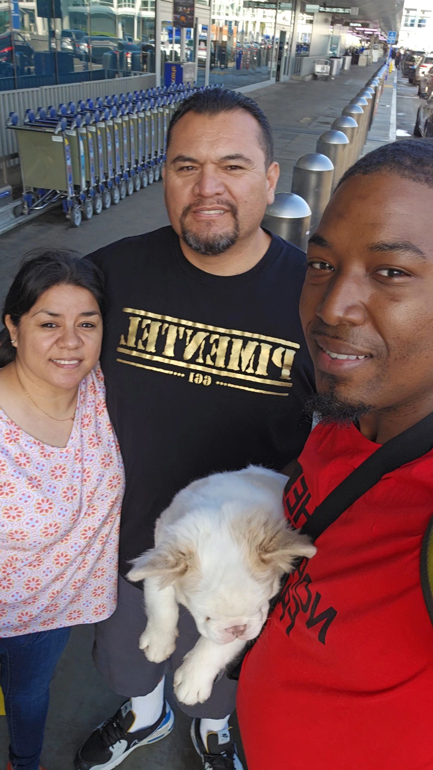 Three people and a puppy outside an airport or shopping center.
