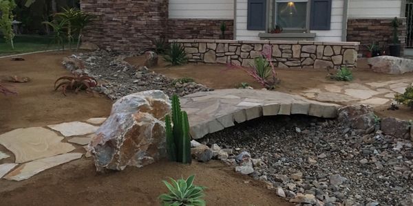 Front yard with DG area broken apart with X shape hardscape flagstone path and river rock. 