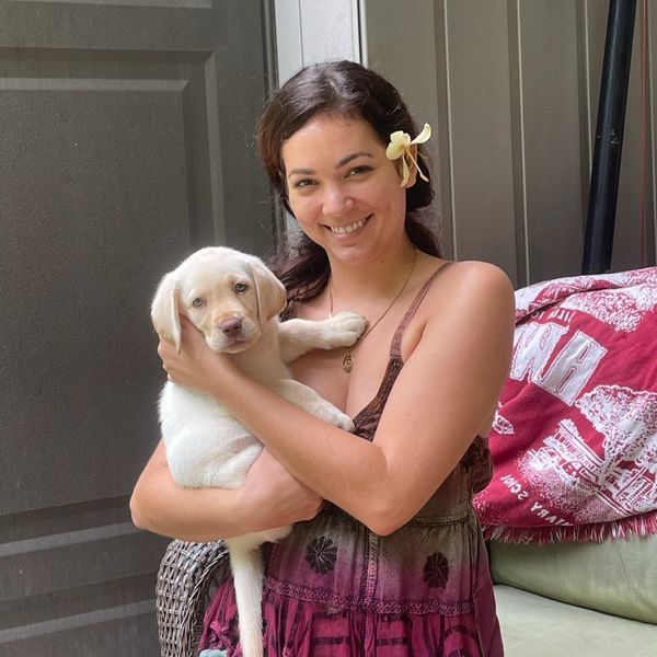 A smiling woman holding a white puppy with a flower in her hair.