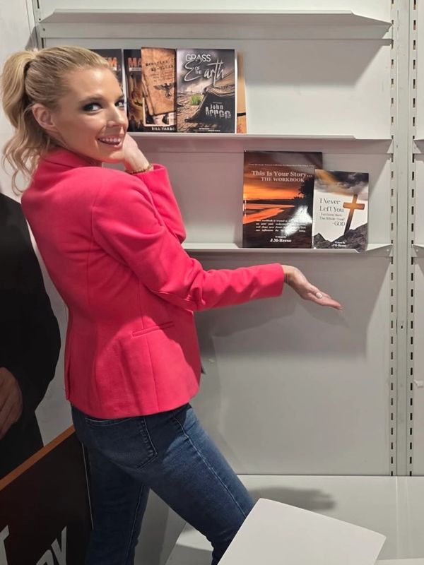Woman in pink blazer showcasing books on a shelf.