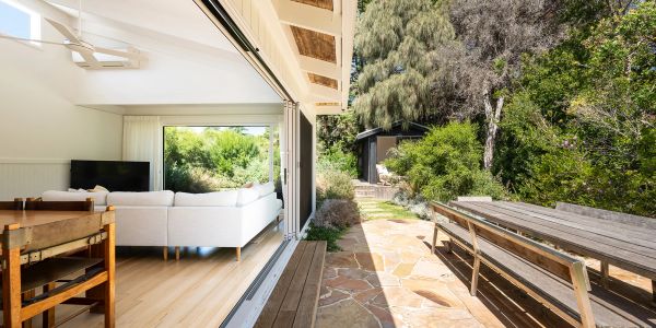 Bright living room opening to sunny outdoor patio with wooden bench table.