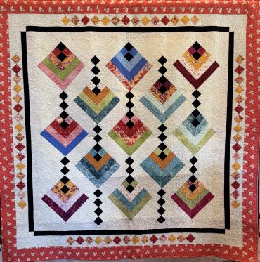 Colorful patchwork quilt with diamond patterns and a pink border.
