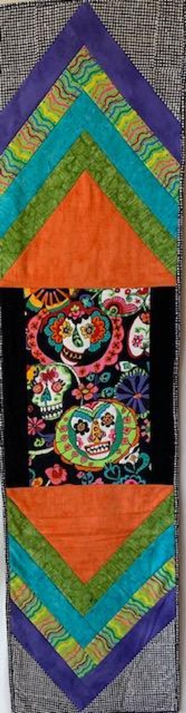 Day of the Dead table runner measures  15 inches wide by 59 inches long; center features colorful "d