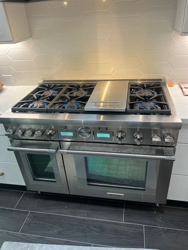 Modern stainless steel stove with six gas burners and dual ovens in a sleek kitchen.