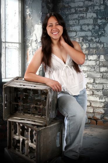 Young woman smiling, leaning on stacked metal boxes in an industrial setting.