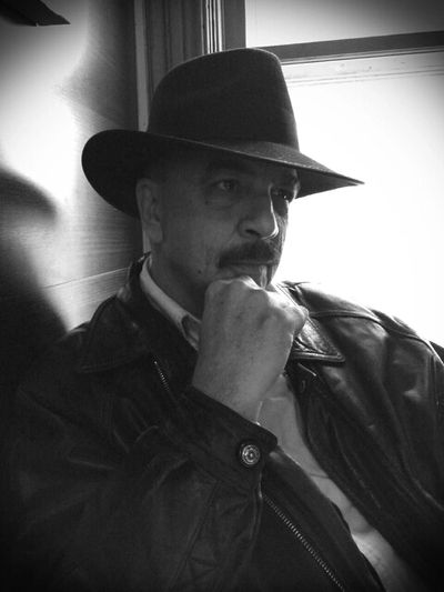 Man in a leather jacket and hat, deep in thought by a window.