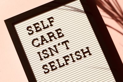 A picture on a wall fallen to one side that says self-care isn’t selfish