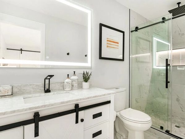 Modern bathroom with illuminated mirror and glass shower enclosure.