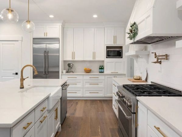 Modern white kitchen with gold fixtures and stainless steel appliances.